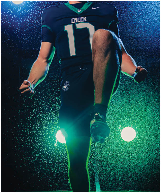 A person wearing a dark sports uniform with the number 17 is energetically raising one knee and clenching fists while shouting, illuminated by bright stage lights and surrounded by a misty atmosphere. Description generated by AI