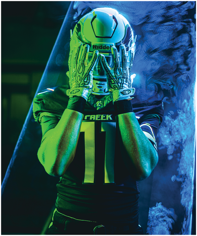 A person with curly hair wearing a dark sports uniform and gloves poses with hands together against a green patterned background. Description generated by AI