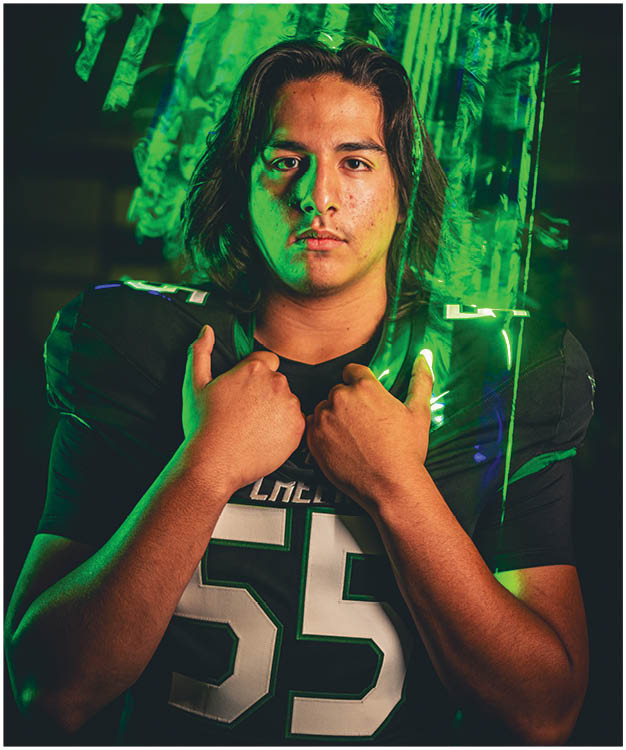 A person wearing a football helmet and jersey with the name “CREEK" and the number 13 is illuminated by green and blue lighting. Description generated by AI