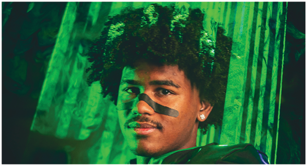 A person with curly hair is partially visible behind green translucent vertical strips in a dimly lit environment. Description generated by AI