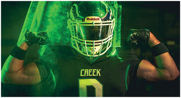 A person wearing a football helmet and uniform stands against a dark background with two bright lights and water droplets creating a dramatic effect. Description generated by AI