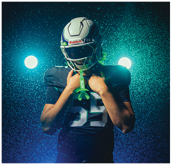 A person wearing a football helmet and jersey with the word Creek and the number 0 flexes their arm in a dramatic green-lit setting. Description generated by AI