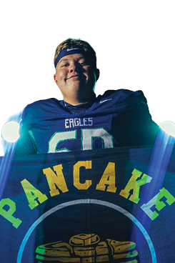 A person wearing a blue sports jersey and headband is holding a blue flag with a stack of pancakes and the word “PANCAKE" written above it. Description generated by AI