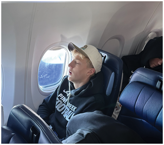 Two people wearing casual clothing and hats are sleeping in adjacent airplane seats near a window. Description generated by AI