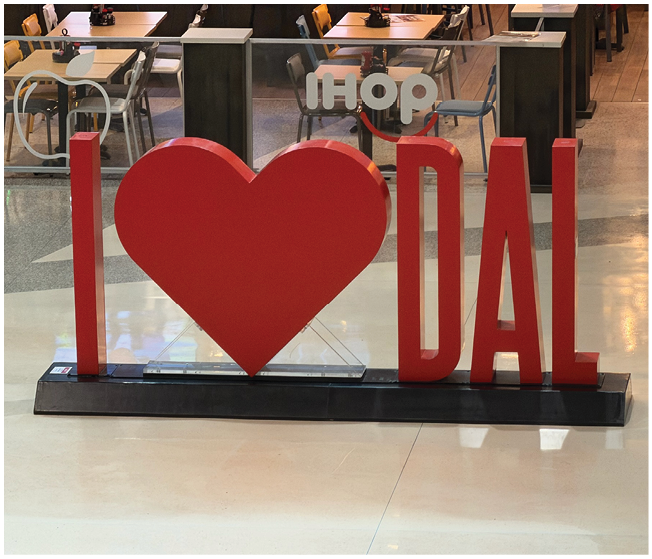 A large red heart sculpture is displayed in front of a glass window with the word “LOVE" in bold red letters and the IHOP logo visible inside the restaurant. Description generated by AI