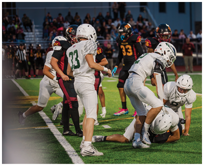 Several people wearing football uniforms are on a field with some players standing and others crouching or lying on the ground during a game. Description generated by AI