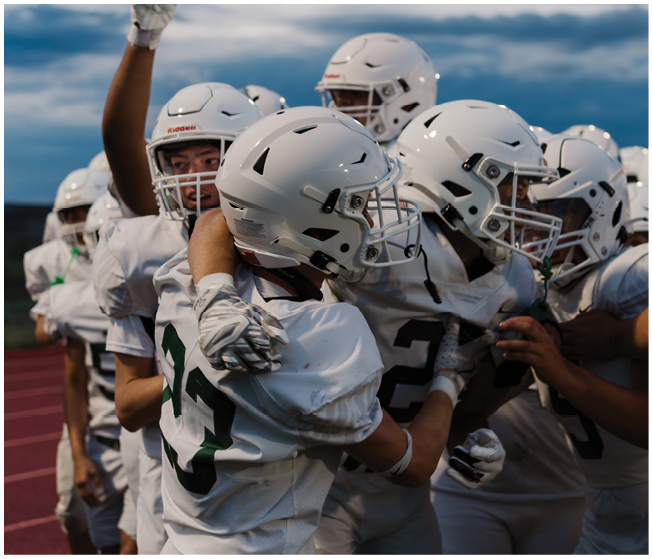 A group of people wearing white football uniforms and helmets are celebrating together on a field during dusk. Description generated by AI