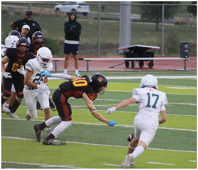 A group of people in sports uniforms are playing football on a field with one person reaching out to catch or intercept the ball. Description generated by AI