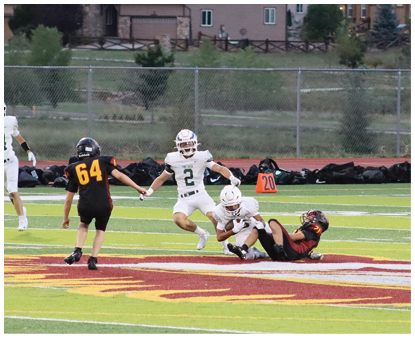 Two people in white sports uniforms are interacting with two people in black and orange sports uniforms on a football field near a yard marker. Description generated by AI