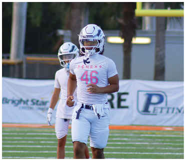 Two people in white football uniforms and helmets are walking on a football field with advertising banners in the background. Description generated by AI