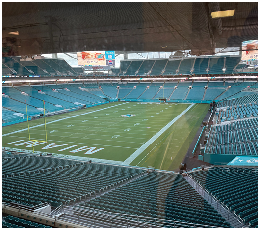 A large empty football stadium with teal seats and a field marked with “MIAMI" near the end zone. Description generated by AI
