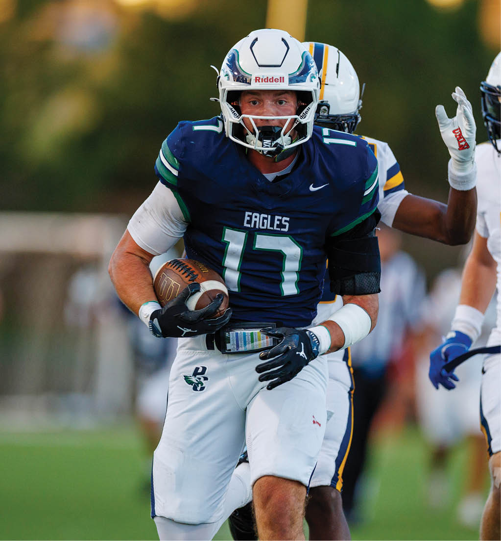 An adult wearing a blue Eagles football uniform with the number 17 is running with a football while being pursued by other players on a field. Description generated by AI