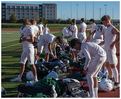 A group of people wearing white athletic clothing are gathered on a sports field with one person holding a folded white shirt. Description generated by AI