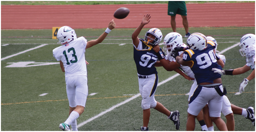 A person wearing a white football uniform is throwing a football while two people in dark blue and white football uniforms attempt to block the pass on a green field. Description generated by AI