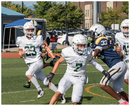 Two people in white football uniforms with helmets are running on a grassy field during a game. Description generated by AI