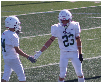 Two people wearing white football uniforms and helmets are on a field, reaching out to touch hands. Description generated by AI