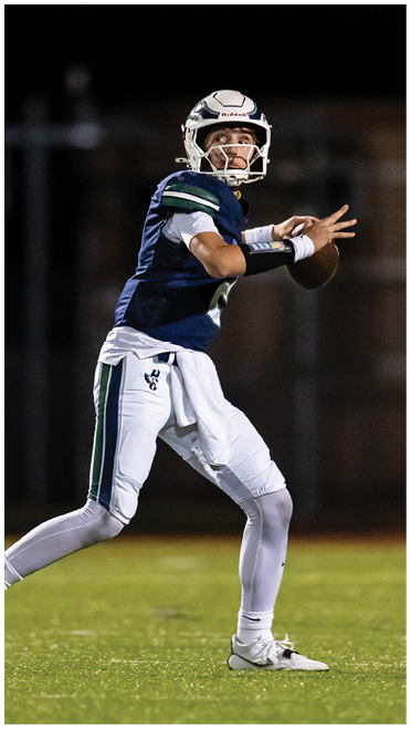 A person wearing a football uniform and helmet is poised to throw a football on a grassy field at night. Description generated by AI