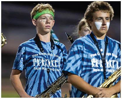 Two people wearing blue tie-dye Pine Creek High School Eagle Marching Band shirts are holding saxophones, with one person having face paint and a green headband. Description generated by AI