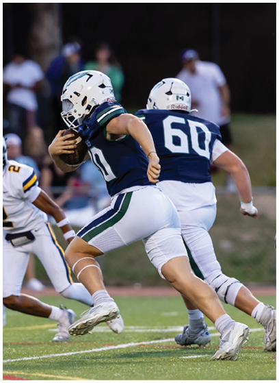 A person in a dark blue and white football uniform is running with the ball while two people in white and yellow uniforms are attempting to catch them on a football field. Description generated by AI