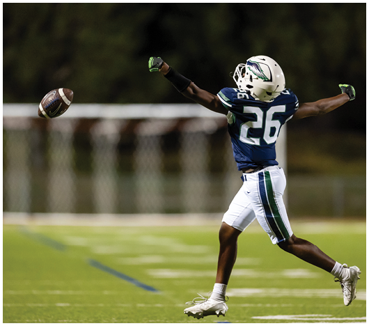 A person wearing a blue and white football uniform with the number 26 is reaching out to catch a football on a grassy field. Description generated by AI