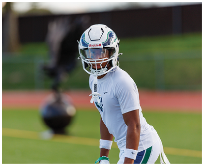 A person wearing a white football helmet and white athletic clothing is standing on a green field, appearing focused and ready for action. Description generated by AI