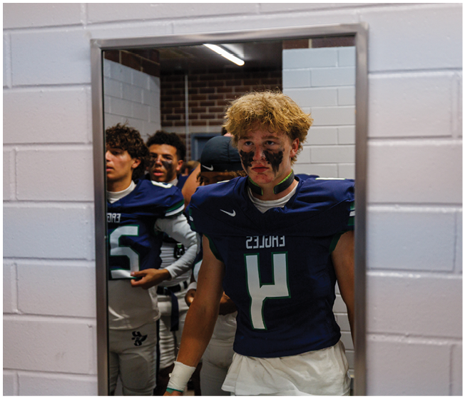 A group of people in football uniforms with face paint are standing in a hallway, with one person in the foreground wearing a number 4 jersey. Description generated by AI