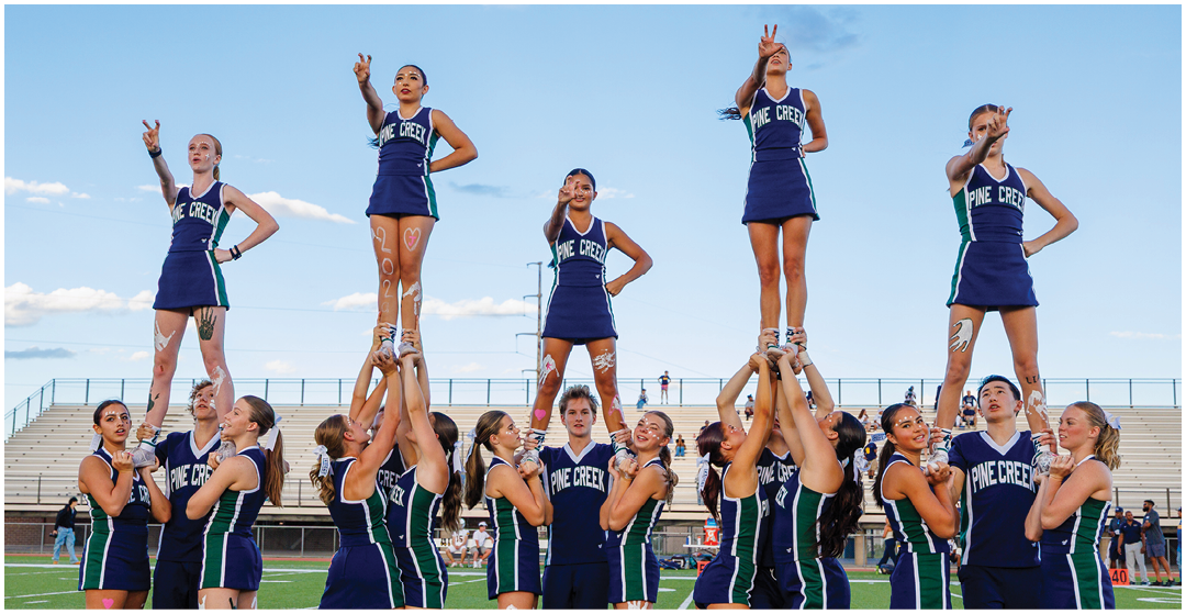 A group of people in matching cheerleading uniforms perform a coordinated stunt on a sports field with some standing on the shoulders of others. Description generated by AI