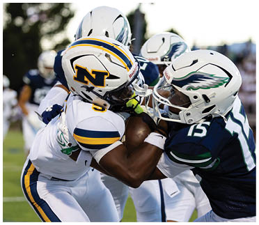 Two football players in helmets and uniforms are engaged in a close physical tackle during a game on a grassy field. Description generated by AI