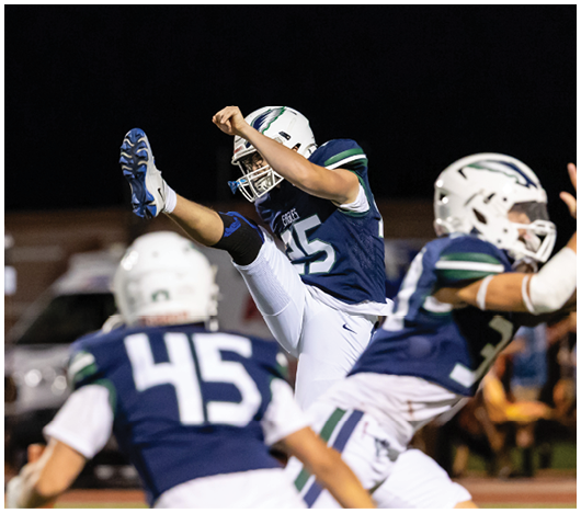 People in football uniforms are on a field at night with one person kicking a ball while others watch or prepare to move. Description generated by AI