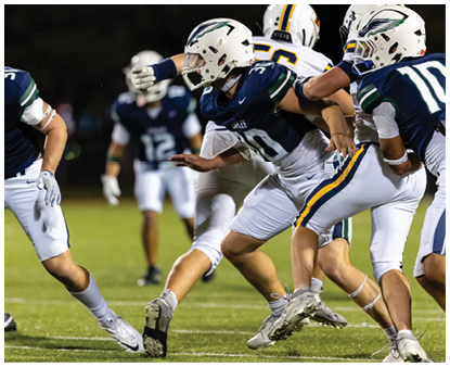 Several people wearing football uniforms and helmets are actively engaged in a play on a grassy field during a game. Description generated by AI