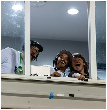 Three people wearing headsets are smiling and leaning over a railing inside a room with large windows. Description generated by AI