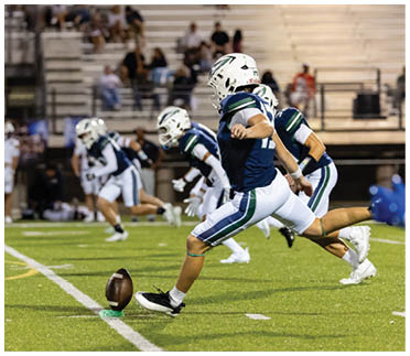 A group of people in football uniforms are on a field with one person kicking a football from a tee during a game. Description generated by AI