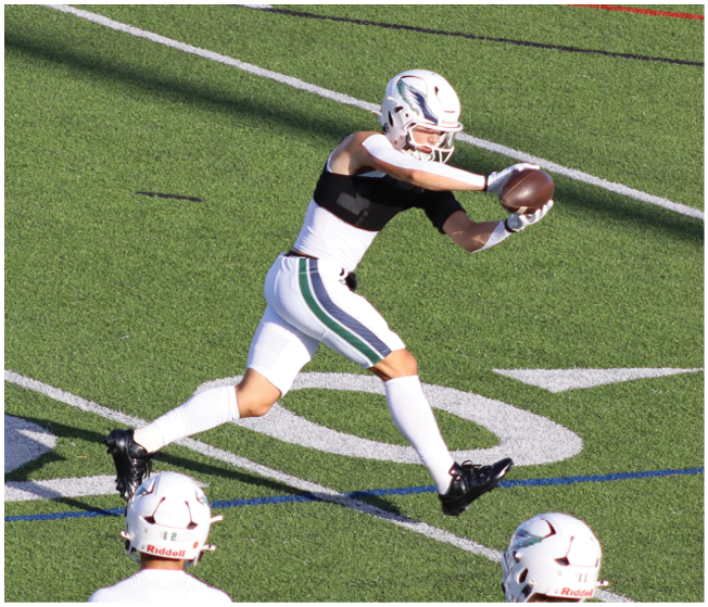 A group of people wearing white football uniforms with red and black accents are sitting and standing closely together on a sports field. Description generated by AI