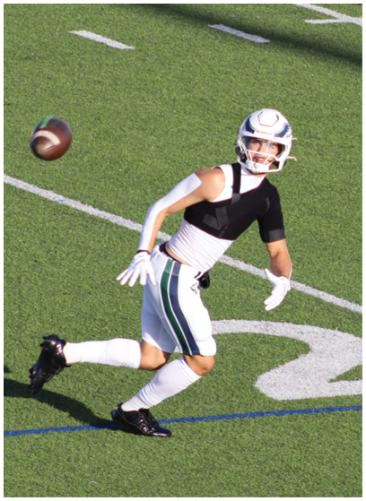 A person in a white football uniform with red accents is holding a football and appears to be running during a game. Description generated by AI