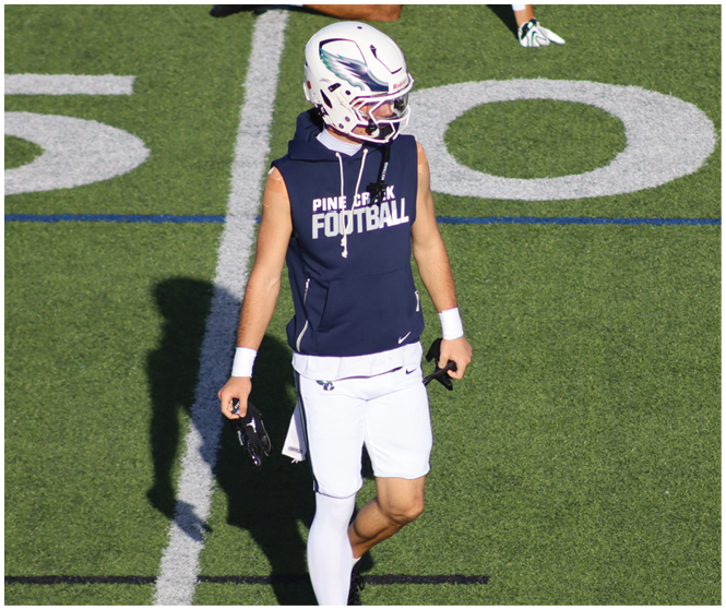 A person in a white football uniform with red accents is holding a football and appears to be running during a game. Description generated by AI