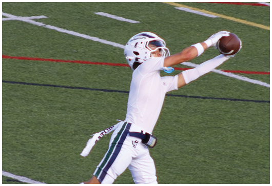 A person in a white football uniform with red accents is holding a football and appears to be running during a game. Description generated by AI