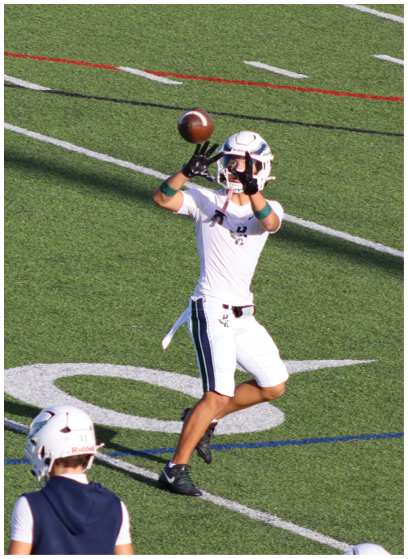 A person in a white football uniform with red accents is holding a football and appears to be running during a game. Description generated by AI