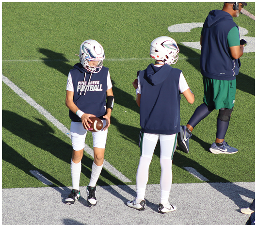 Two people wearing white football helmets with red faceguards and a red lion logo are focused and looking ahead. Description generated by AI