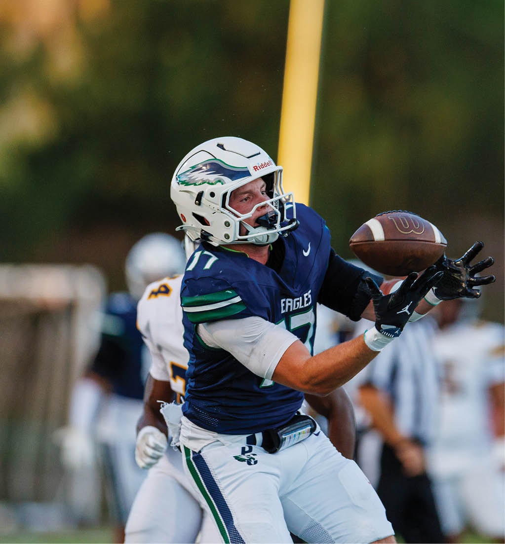 A person wearing a football uniform and helmet is reaching out with both hands to catch a football during a game. Description generated by AI