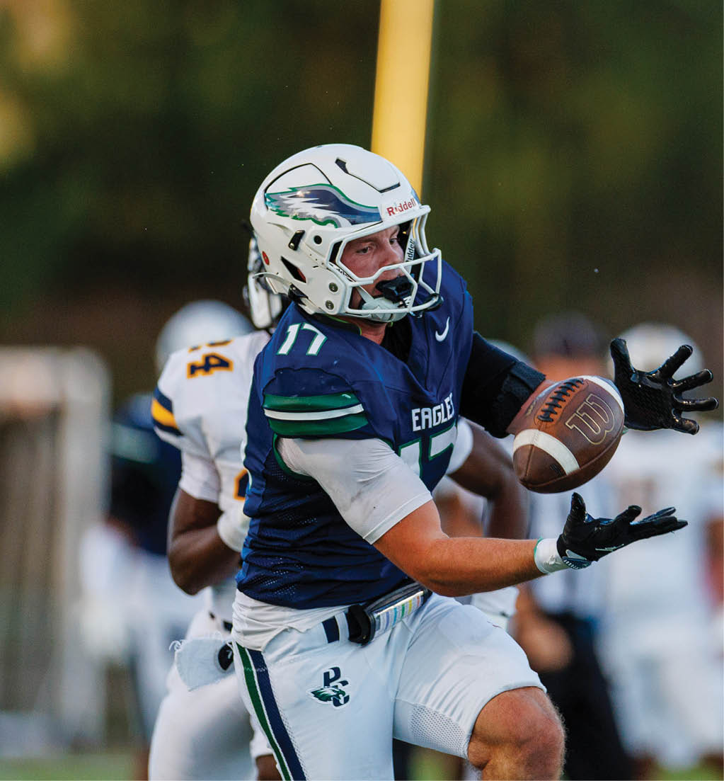 A person wearing a blue football uniform with the number 17 and a white helmet is catching a football during a game with another player in a white uniform behind them. Description generated by AI