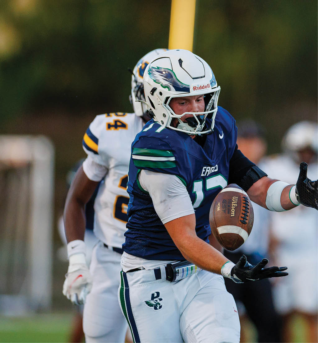 A person in a blue and white football uniform is catching or holding a football while another person in a white and yellow uniform is behind them on a field. Description generated by AI
