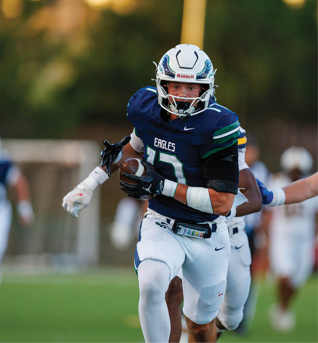 A person wearing a blue and white football uniform with the word Eagles on the jersey is running on a field while holding a football. Description generated by AI