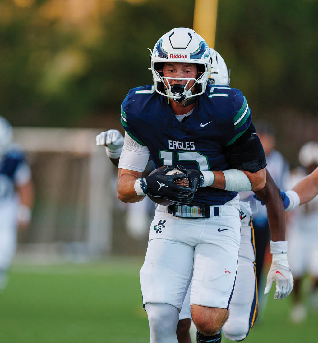 A person wearing a blue and white football uniform with the word Eagles on the jersey is holding a football while being closely pursued by another player on a grassy field. Description generated by AI