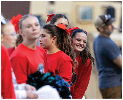 A group of people wearing red shirts and red hair bows stand together, with one person smiling brightly while others appear more neutral. Description generated by AI