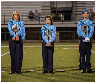 Three people in matching blue and black marching band uniforms stand on a football field holding brass instruments. Description generated by AI