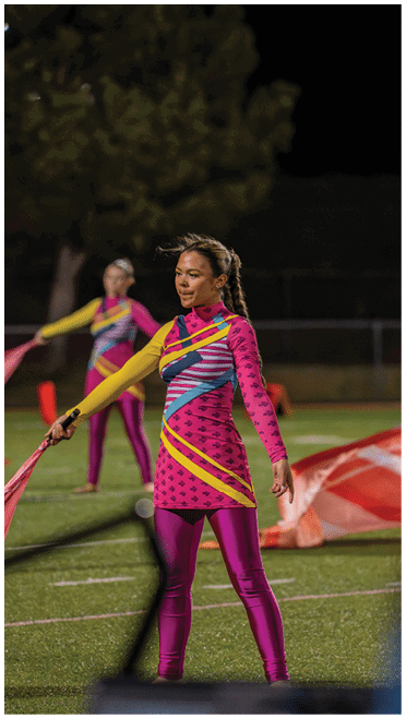 People in colorful uniforms perform a flag routine on a sports field at night. Description generated by AI