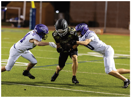 A group of people wearing camouflage-patterned football uniforms and helmets are standing together on a lit football field at night. Description generated by AI