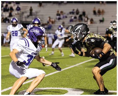 A group of people wearing camouflage-patterned football uniforms and helmets are standing together on a lit football field at night. Description generated by AI