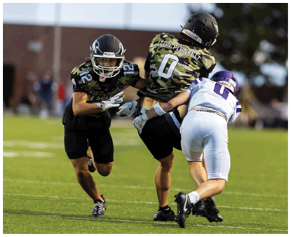 A group of people wearing camouflage-patterned football uniforms and helmets are standing together on a lit football field at night. Description generated by AI