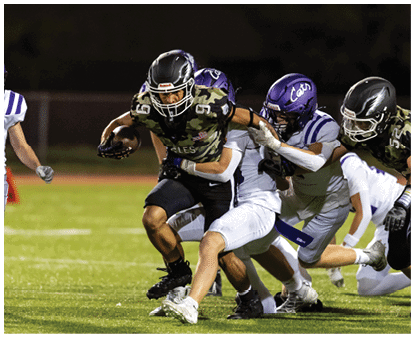 A group of people wearing camouflage-patterned football uniforms and helmets are standing together on a lit football field at night. Description generated by AI